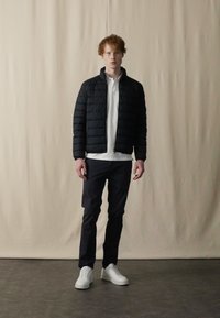 Black puffer jacket, white collared shirt, navy pants, and white sneakers. The fabric is smooth; the design is modern and fitted.