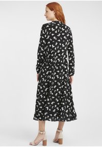 Schwarzes Blumenkleid mit langen Ärmeln, gestuftem Design, weißem Blumenmuster und rundem Halsausschnitt. Getragen mit beigen Riemchenabsätzen.