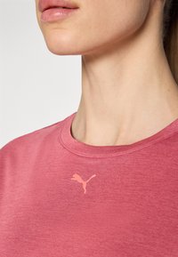 Vaaleanpunainen urheilupaita, jossa on pyöreä pääntie ja vaaleanpunainen Puma-logo vasemmassa ylärinnassa. Pehmeä, teksturoitu kangas.