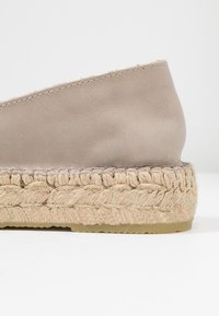 Espadrilla beige con una toma superiore liscia e morbida, piattaforma in juta intrecciata e una sottile cucitura lungo il bordo superiore.