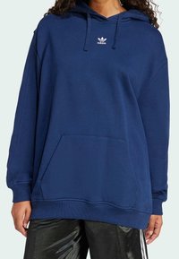 Sudadera de color azul marino hecha de un tejido suave, con un bolsillo canguro, capucha con cordones y el logo blanco de Adidas en el pecho.