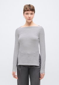 Hosszú ujjú, csónaknyakú felső fehér alapon fekete vízszintes csíkokkal. Laza szabású, oldalán hasítékokkal a könnyű mozgásért.