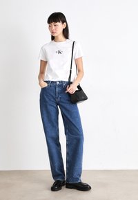Witte katoenen t-shirt met een klein zwart logo, gecombineerd met losse blauwe denim jeans en een kleine zwarte leren schoudertas. Zwarte schoenen maken de look compleet.