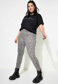 Jeans grigi con motivo a leopardato sottile, abbinati a una t-shirt nera a maniche corte con scritte bianche, e stivaletti neri da combattimento.