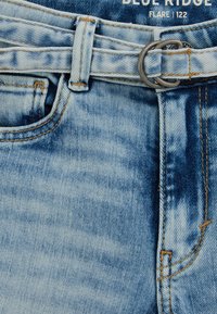 Helesinised teksapüksid tuhmunud tekstuuriga, millel on vöö hõbedase metallist pandlaga ja kontrastse oranži õmblusega.