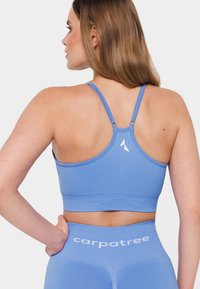 Sport bra in light blue, made of smooth fabric. Features adjustable thin straps, a subtle logo, and a fitted design, suitable for activewear.