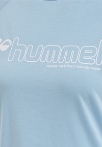 Jasnoniebieska bawełniana koszulka z okrągłym dekoltem, z dużym białym logo i napisem "ZMIEŃ ŚWIAT POPRZEZ SPORT."