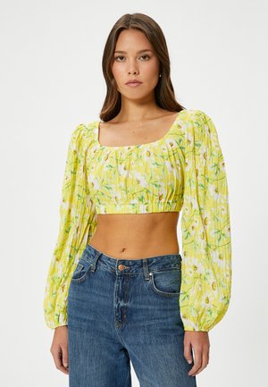 Gezellig geel bloesje met cropped lengte, pofmouwen en vierkante halslijn. Geweven stof met groene en witte bloemenpatronen. Draagt met hoge taille jeans.
