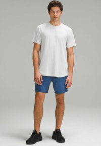 Weißes kurzärmeliges Hemd, blaue Shorts, schwarze Schuhe. Das Hemd hat einen Rundhalsausschnitt; die Shorts haben Taschen; der Stoff scheint leicht zu sein.