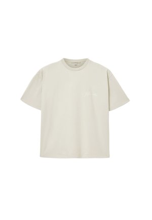 T-shirt en coton beige clair avec un col rond, des manches courtes, et un logo blanc discret sur le côté gauche de la poitrine. Texture lisse.