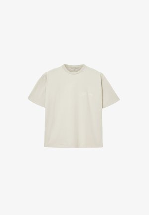T-shirt en coton beige clair avec un col rond, des manches courtes, et un logo blanc discret sur le côté gauche de la poitrine. Texture lisse.