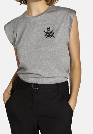 Harmaa, hihaton puuvillainen t-paita, jossa musta graafinen kuvio edessä, yhdistetty mustiin räätälöityihin housuihin.