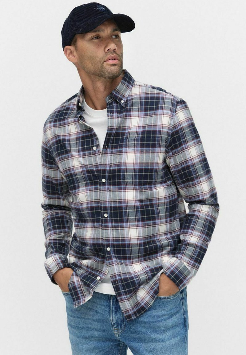 Heren flanellen overhemd in donkerblauw, wit en bordeaux geruit patroon. Button-down kraag, lange mouwen, gecombineerd met een eenvoudig wit T-shirt eronder.