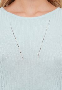 Ανοιχτό μπλε πλεκτό πουλόβερ με κάθετες ραβδώσεις και μικρές λεπτομέρειες με κοψίματα που σχηματίζουν σχήμα V στο εμπρόσθιο μέρος του λαιμού. Απαλή υφή.