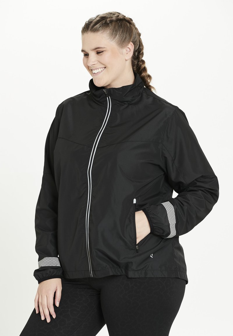 Svart zip-up jacka med hög krage, vit kant och texturerade ärmslut. Har sidofickor och elastiska handleder för en säker passform.