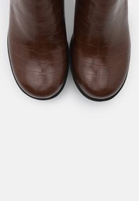 Botas de tobillo de cuero marrón con una textura de grabado de cocodrilo y punta redonda, con una suela de goma negra para mayor agarre.