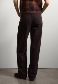 Donkerbruine, brede broek gemaakt van een zachte stof, met achterzakken en een relaxte pasvorm. Gemaakt in combinatie met een kleurrijke, gestructureerde top.
