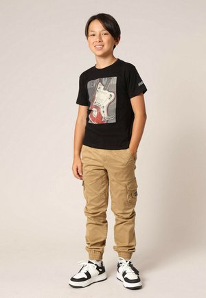 Zwarte t-shirt met een gitaarafbeelding, beige cargobroek met zijzakken en zwart-witte sneakers met veters.