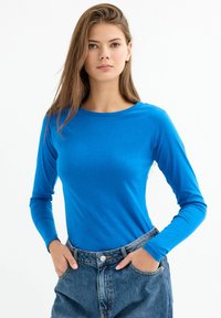 Camisa azul de manga larga hecha de tela suave con un cuello redondeado, combinada con shorts de mezclilla de cintura alta. El conjunto tiene un ajuste casual.