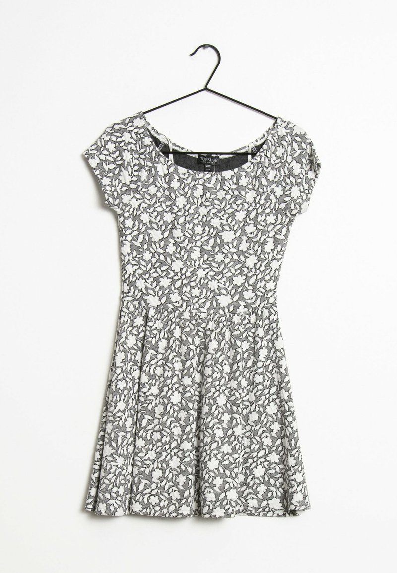 Schwarz-weißer, floral gemusterter Kurzarmkleid mit rundem Ausschnitt und ausgestellt Rock, gefertigt aus weichem Stoff, hängt an einem Haken.