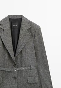 Grau gewobener Blazer mit strukturiertem Kragen, schwarzen Knöpfen und einem Gürtel mit Metallölöchern, kombiniert mit einer Brusttasche.