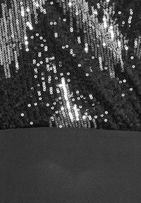 Svart tyg prytt med glittrande silverpaljetter som skapar en glittrande textur som övergår till en slät kontrasterande nederdel.