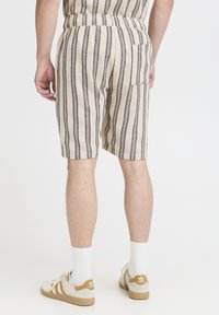 Striped beige shorts with black vertical lines, elastic waistband, and a back pocket; worn with white socks and beige sneakers.