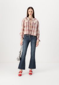 Blusa a maniche lunghe in plaid rosa e bianco con colletto in pizzo, abbinata a jeans svasati scuri e sandali con tacco rossi. Tiene una borsa argentata.