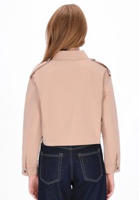 Giacca beige ritagliata con colletto classico e spalline, con polsini abbottonati e una texture liscia e opaca.