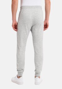 Grå sweatsbukser lavet af blødt stof, med elastisk talje og tapered manchetter, sammen med hvide sneakers.