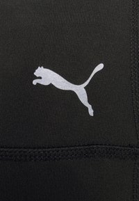 Czarna tkanina sportowa wyróżnia się wyraźnym srebrnym logo Pumy. Materiał ma gładką fakturę z płaskimi szwami i starannym wykończeniem.