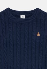 Navy blue cable-knit sweater with a ribbed neckline and an embroidered bear logo on the left chest. Soft texture with vertical patterns.