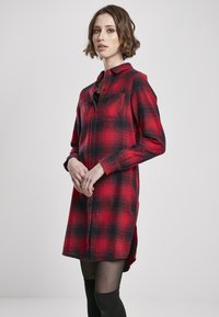 Robe chemise en flanelle à carreaux rouges et noirs, avec un col, une fermeture à boutons, deux poches poitrine et des manches longues. Tissu texturé.