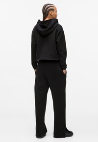 Hanorac scurt de culoare neagră, cu glugă, având manșete și tiv cu nervuri, asortat cu pantaloni largi negri. Ambele sunt realizate dintr-un material moale, texturat.