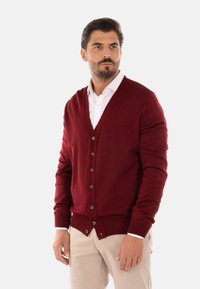 Cardigan lavorato a maglia rossa con scollo a V, chiusura con bottoni e polsini a coste. Presenta una texture liscia e cinque bottoni per la chiusura.