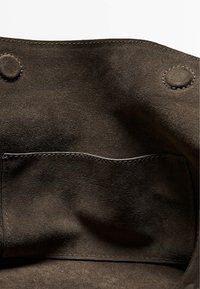 Dark brown suede interior of a bag showing a stitched pocket and two round magnetic snap closures.