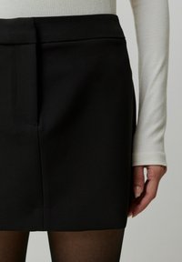 Zwarte minirok met een soepele textuur en een aansluitende tailleband, voorzien van een enkele frontzak en een rechte snit, gedragen met een lichtblauw langemouwen top.