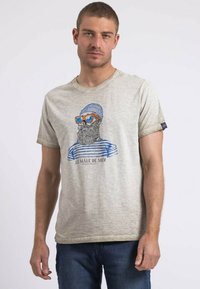 T-shirt en coton gris clair avec un col rond, présentant un graphique d'un homme barbu portant des lunettes de soleil et un bonnet en tricot bleu, avec un motif rayé.
