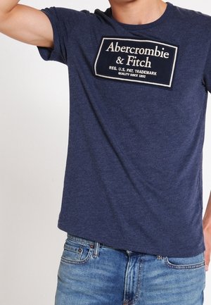 Granatowa bawełniana koszulka z krótkim rękawem, z okrągłym dekoltem, z prostokątną białą naszywką z napisem "Abercrombie & Fitch".