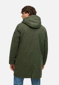 Zelen parka s kapuco, gladke teksture, dolgim silhuetom in stranskimi žepi; ima šiv po hrbtu in označen logo.