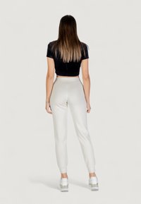 Top corto in velluto nero e pantaloni jogger slim-fit grigio chiaro con caviglie elastiche, abbinati a sneakers bianche con dettagli metallici.