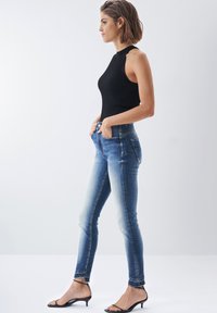 Top de tirantes de canalé oscuro combinado con unos vaqueros de tiro alto de color azul, que presentan un efecto ombré desvaído y un corte hasta el tobillo, acentuados con costuras sutiles.