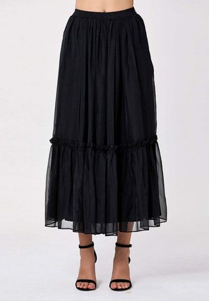 Jupe midi noire avec taille froncée et volant, portée avec des sandales à talons hauts noires avec bride à la cheville.