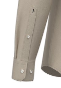 Beige textuur van een lange mouw shirtmanchette met drie witte knopen en een kleine zwart geborduurde roos boven de sluiting.