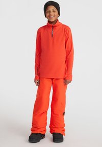 Ljusorange fleece-tröja med halvhög krage, matchad med orange byxor. Har svarta accenter och hållbara svarta stövlar.