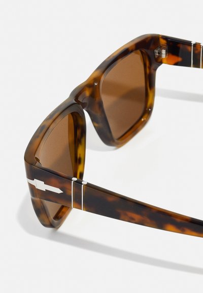 Γυαλιά ηλίου από χελώνα με καφέ φακούς. Ορθογώνιο σχήμα, χοντρά πλαίσια, ασημένιες λεπτομέρειες στους βραχίονες, λεία υφή.