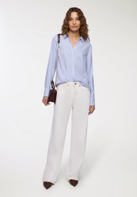 Camicia a righe blu chiaro e bianca con bottoni, abbinata a pantaloni bianchi a gamba larga e scarpe beige a punta. Piccola borsa bordeaux.