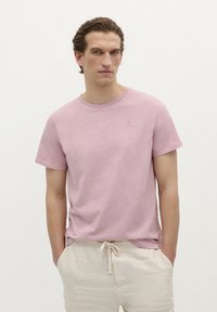 Lyserød bomulds T-shirt med rund halsudskæring og korte ærmer; har et lille logo på brystet; parret med beige snoretræk shorts.