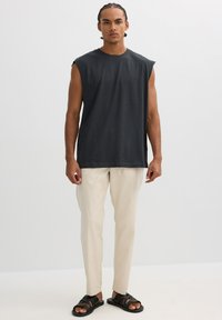 Camiseta sin mangas de color gris oscuro, pantalones cremosos ajustados y sandalias negras. El tejido parece suave; la camiseta presenta un corte holgado y un diseño minimalista.