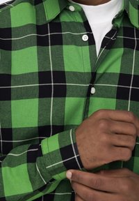 Grün-schwarz kariertes Hemd, aus Baumwolle, mit Knopfleiste, weißen Knöpfen, sichtbarem Kragen, langen Ärmeln mit Manschetten, feinem Karomuster.